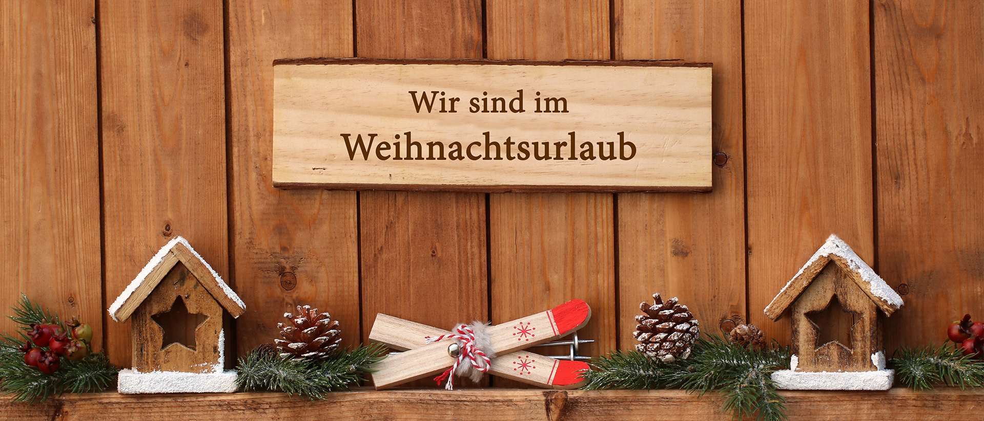 Schild mit Hinweis zum Weihnachtsurlaub an Holzwand mit Weihnachtsdeko